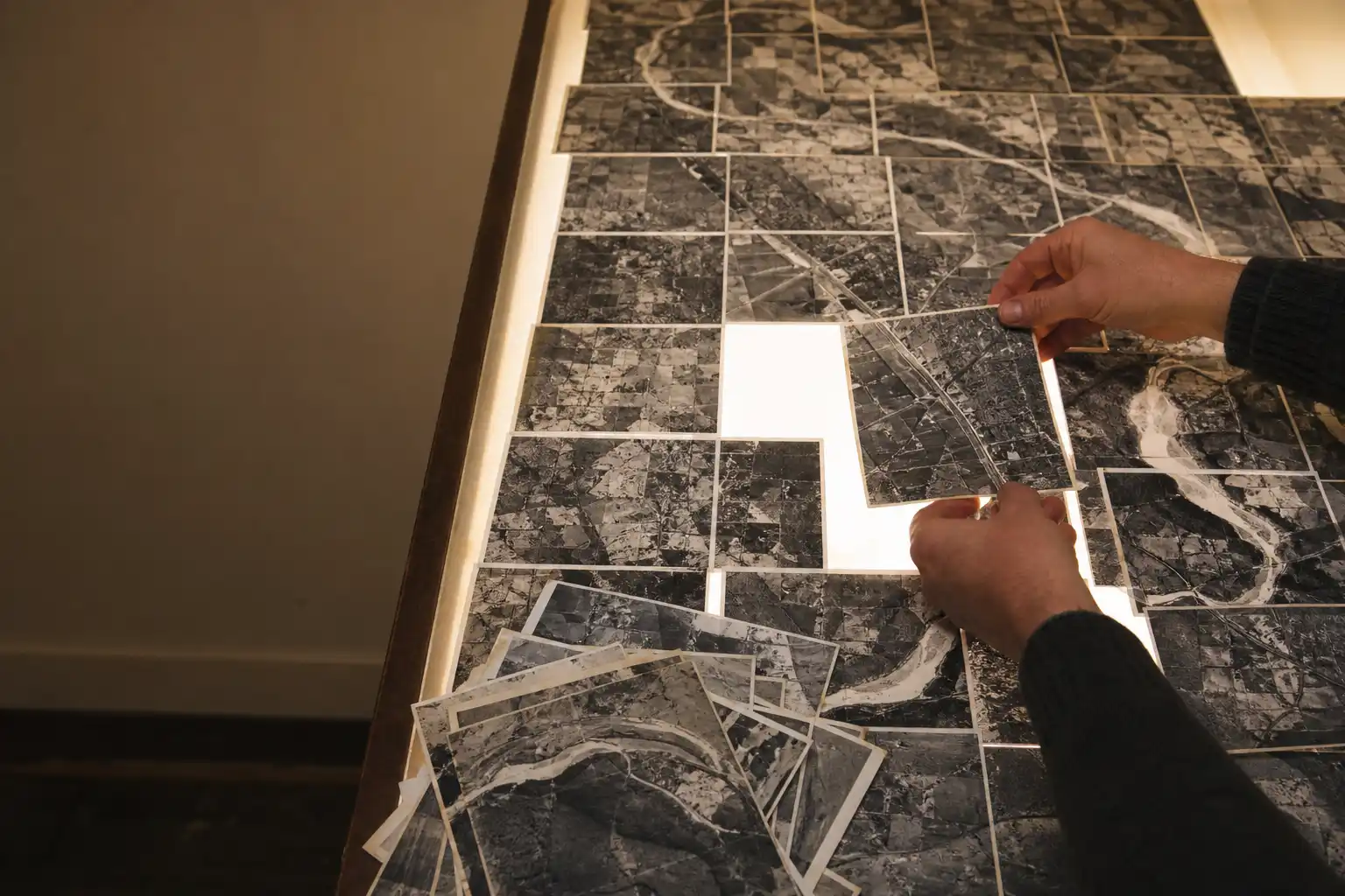 Hands laying overlapping aerial photograph prints edge to edge on a light table so the roads join across them